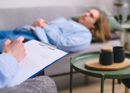A therapist taking notes during a session with a patient lying on a sofa indoors.